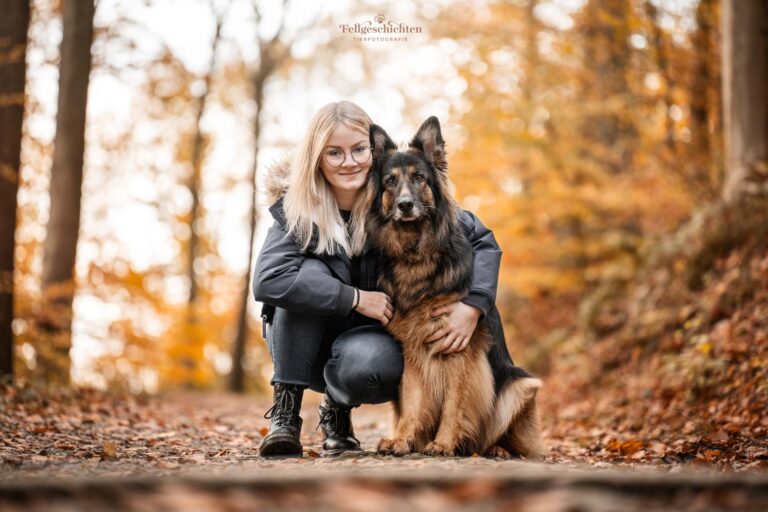 Junge Frau hockt neben einem Schäferhund im herbstlichen Wald