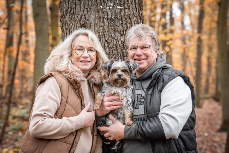 Ehepaar mit Yorkshire Terrier auf dem Arm lehnt an einem Baum