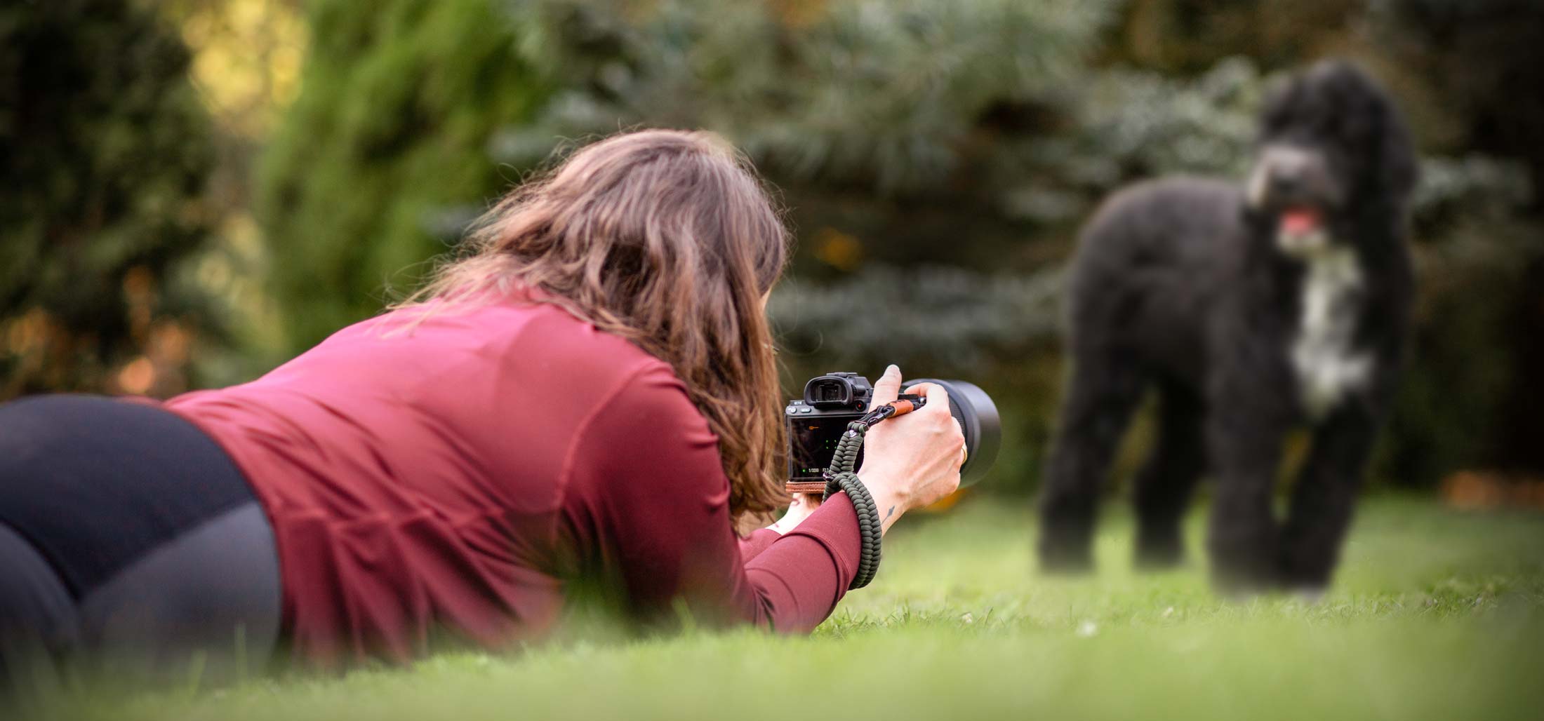 Frau liegt auf dem Boden und fotografiert einen Hund