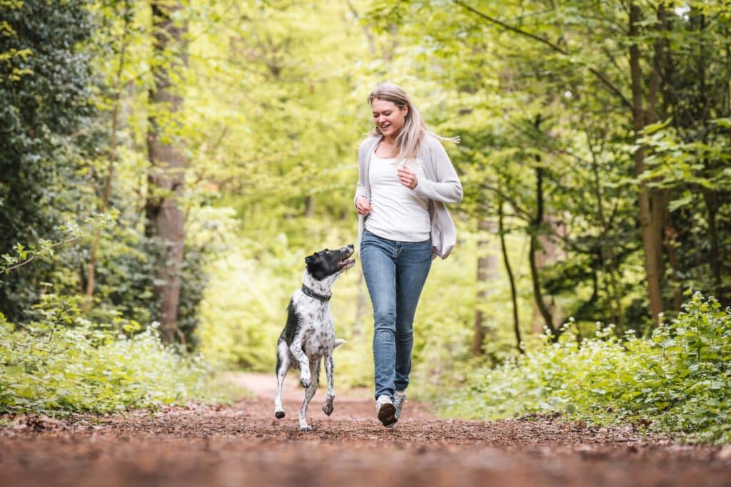 Frau rennt mit Hund durch einen Wald