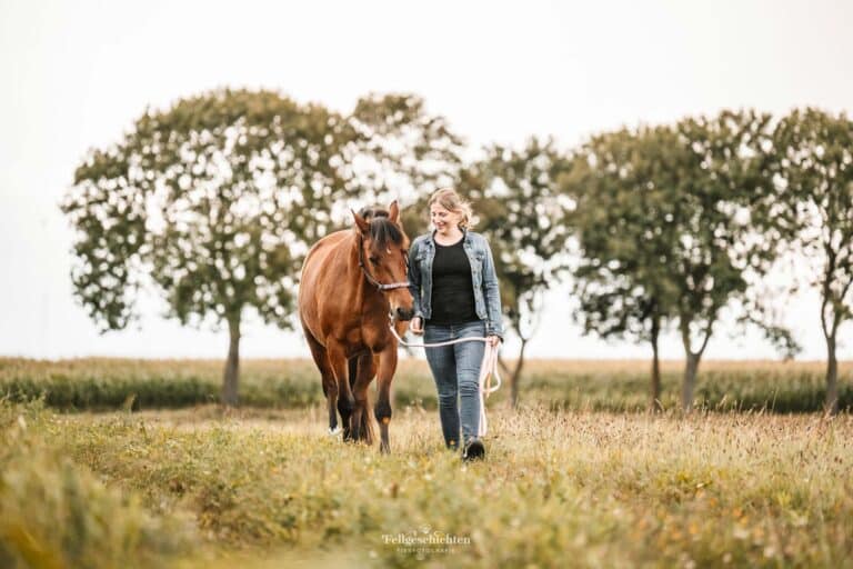Frau läuft mit ihrem Pferd über eine Wiese